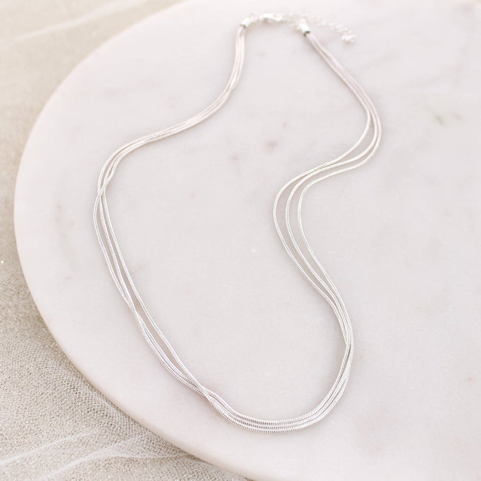Silver three-strand snake chain necklace displayed on a white marble background.