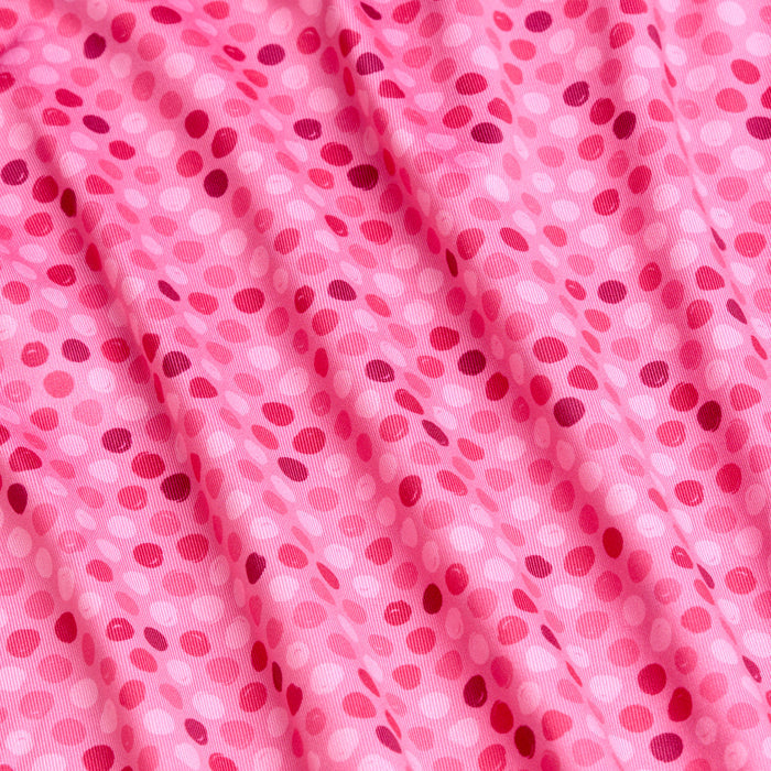 The Dots - Pink - Polo features soft, moisture-wicking pink fabric with small, scattered dots in shades of pink and red. Gentle folds create subtle shadows and highlights, adding depth and texture to the design.
