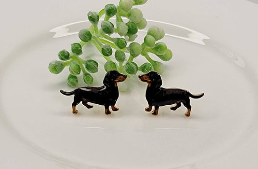 Two small black dog figurines on a white surface with green leaves in the background.