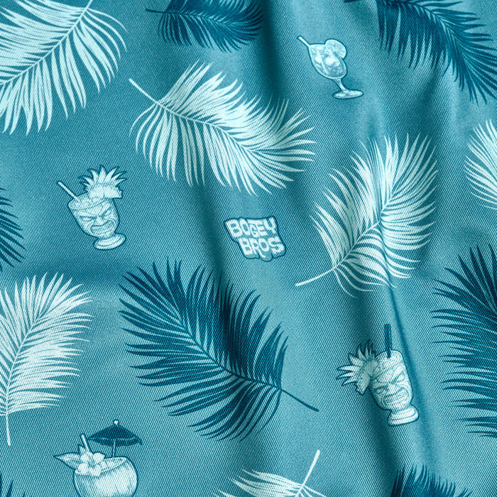 The Boat Drinks - Polo features a teal fabric with tropical palm leaves, colorful cocktails (some with umbrellas or fruit), and playful white "BUBBY BROS" text. This athletic-fit polo offers UPF 50 protection for sunny adventures.