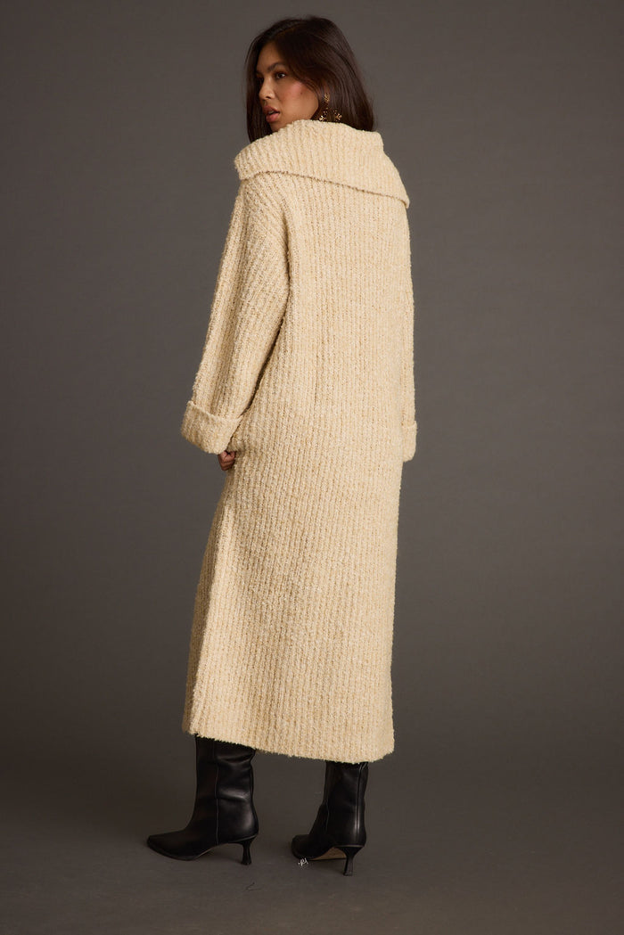 Back of the Cassia cream knit long cardigan coat, shawl collar and ankle-length hem with black boots.