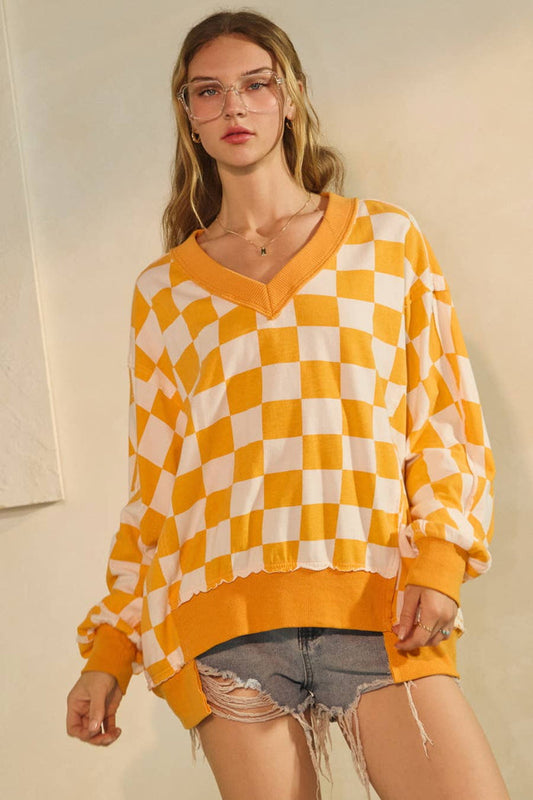 Woman wearing a yellow and white checkered sweater with ripped denim shorts against a neutral background