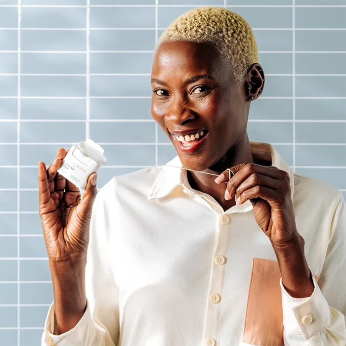 Woman holding a Boka Cinna Mint Floss against a tiled wall background