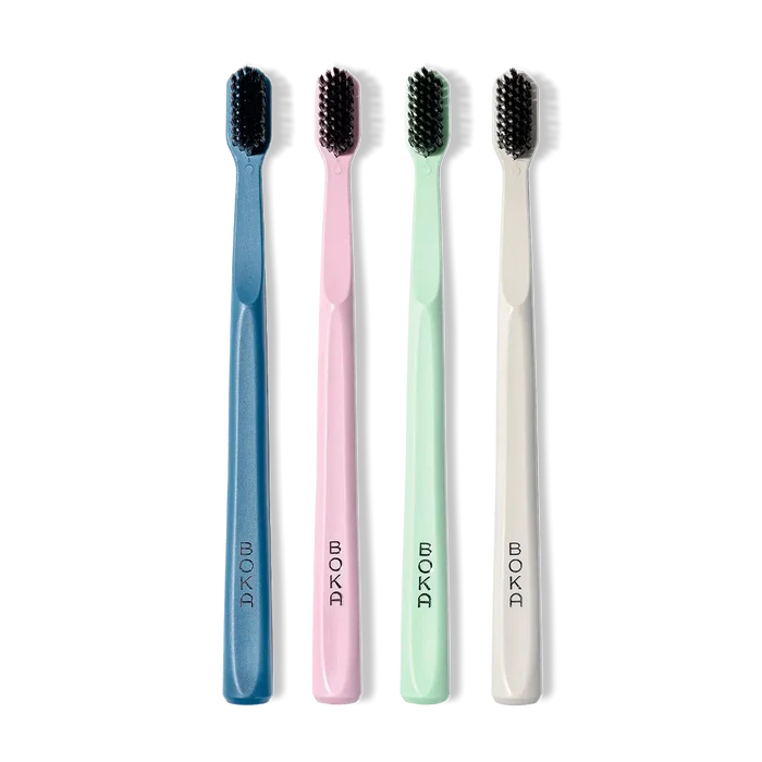 Four toothbrushes in blue, pink, green, and white with black bristles on a white background.