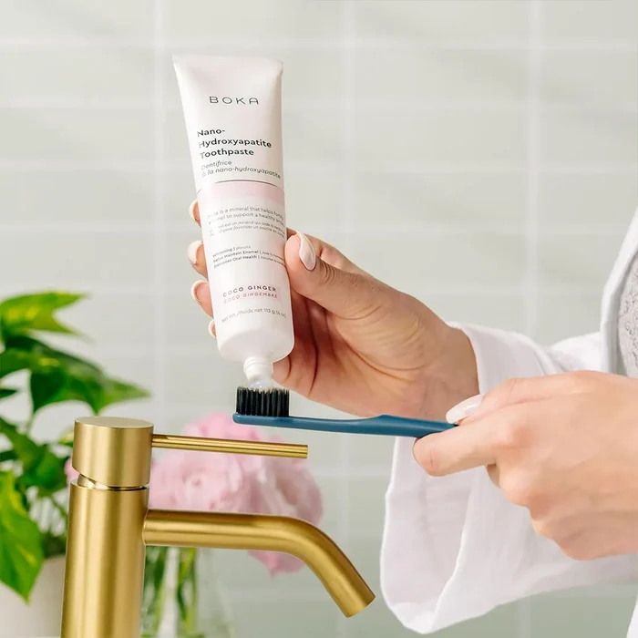 Person applying toothpaste to a toothbrush with a Boka toothpaste tube in a bathroom setting.