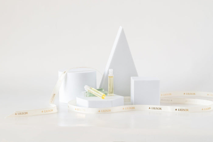A sample bottle of LILIXIR Ageless Rejuvenating Serum placed on a white stand with a geometric design, surrounded by recyclable packaging marked with 'LILIXIR'.