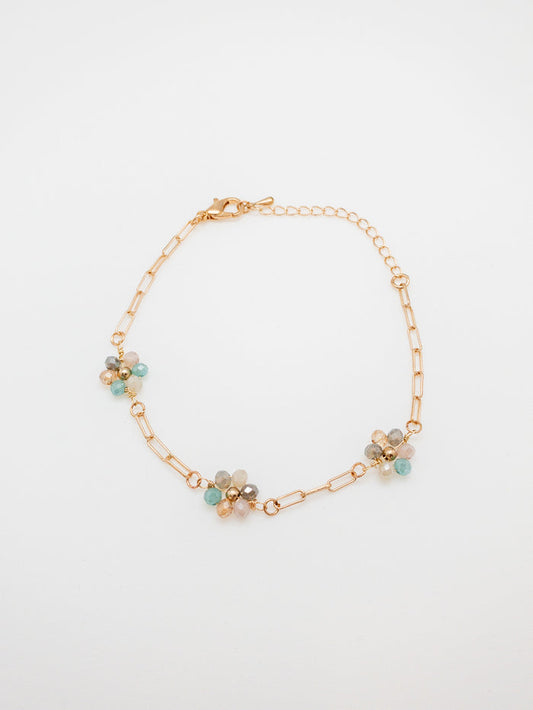 A gold-plated bracelet with multicolored daisy-shaped clusters on a white background.