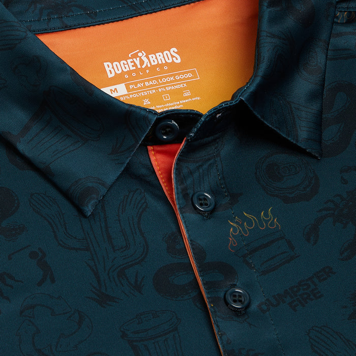 Close-up of the Deep Trouble - Polo, a dark teal button-up shirt with a playful cacti, burger, and flames pattern. It features an athletic fit, moisture-wicking fabric, orange collar lining, and the phrase DUMPSTER FIRE faintly visible.