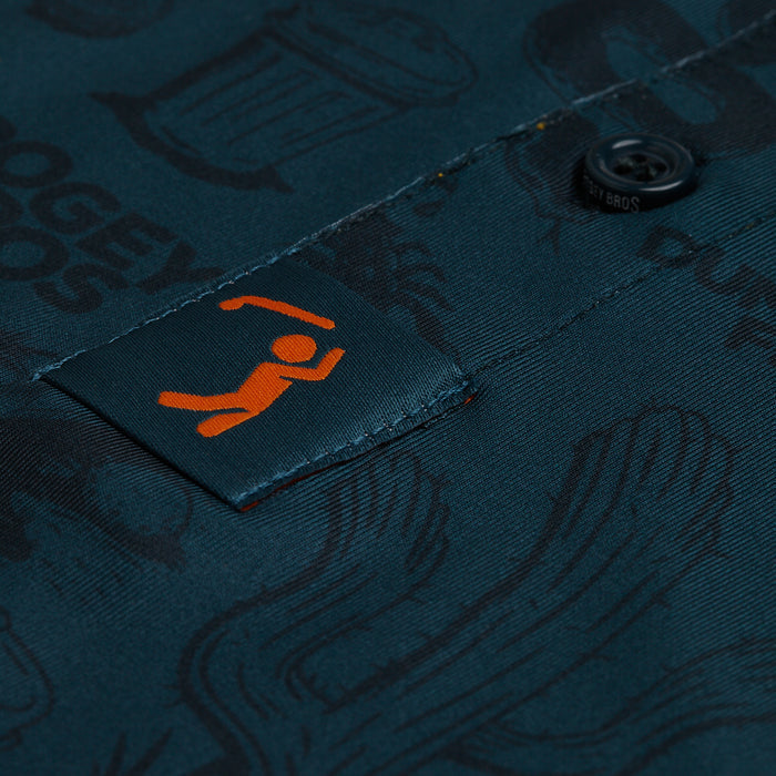 Close-up of the Deep Trouble - Polo in dark teal with black graphics and text, athletic fit. Features a placket button and a fabric tab with an orange stick figure near the button, highlighting its subtle, playful design.