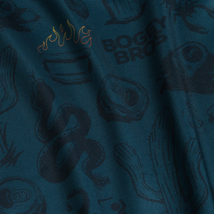 A close-up of the Deep Trouble - Polo shows dark teal fabric with black and colorful cartoon prints—snake, cactus, and steak. The athletic fit material appears slightly wrinkled, adding soft shadows and visual texture for a dynamic look.