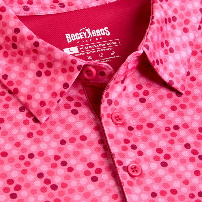 A close-up of the Dots - Pink - Polo, featuring a pink polka dot pattern, athletic fit, three pink buttons, moisture wicking, UPF 50 protection, and made from polyester and spandex by Bogey Bros.