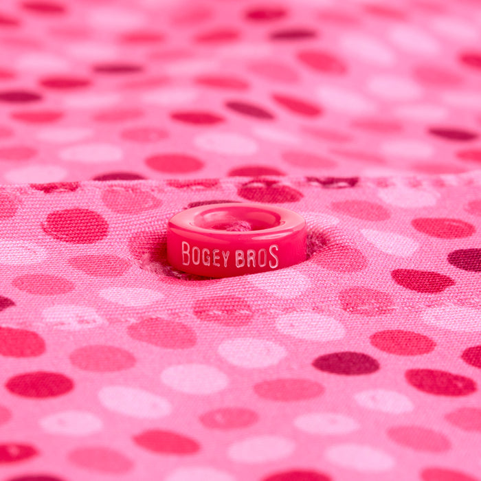 A small pink ring with BOGEY BROS in white rests on the Dots - Pink - Polo, featuring shaded polka dots that match the vibrant style and moisture-wicking athletic fit of their apparel. The ring stands out against the playful polo design.