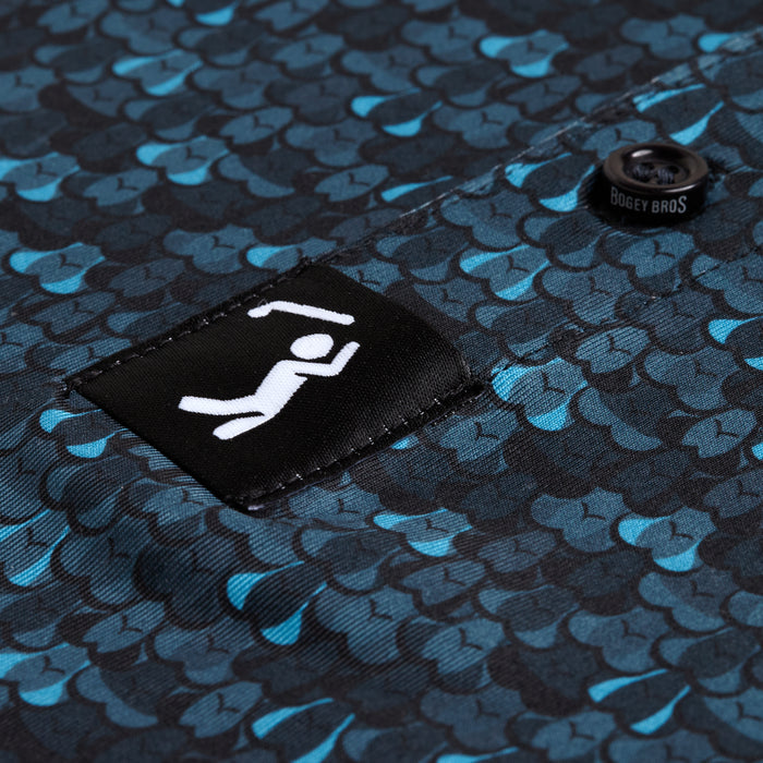 Close-up of Eyes Up Here - Zapped - Polo’s blue and teal fish scale patterned, moisture-wicking fabric and black patch with a white stick figure lifting a barbell, keeping you cool and dry during any activity.