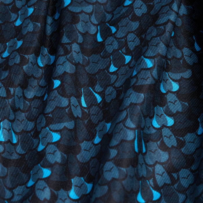 Close-up of the Eyes Up Here - Zapped - Polo fabric shows overlapping blue and turquoise fish scale shapes on black. The slightly wrinkled, moisture-wicking material adds depth and comfort to this bold design.