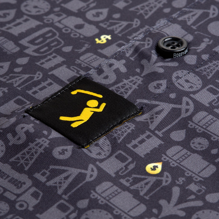 The Gusher - Polo is a dark shirt with gray oil industry icons, athletic fit, and moisture-wicking fabric. A black tag with a yellow figure lifting a bar is stitched by the black BOGEY-labeled button.