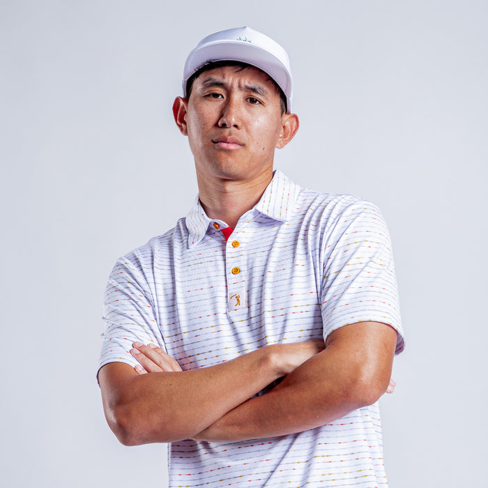 A man wearing the Heat Index - Polo, a light short-sleeve collared shirt with multicolored stripes and an athletic fit, stands with his arms crossed, looking at the camera against a plain light gray background.
