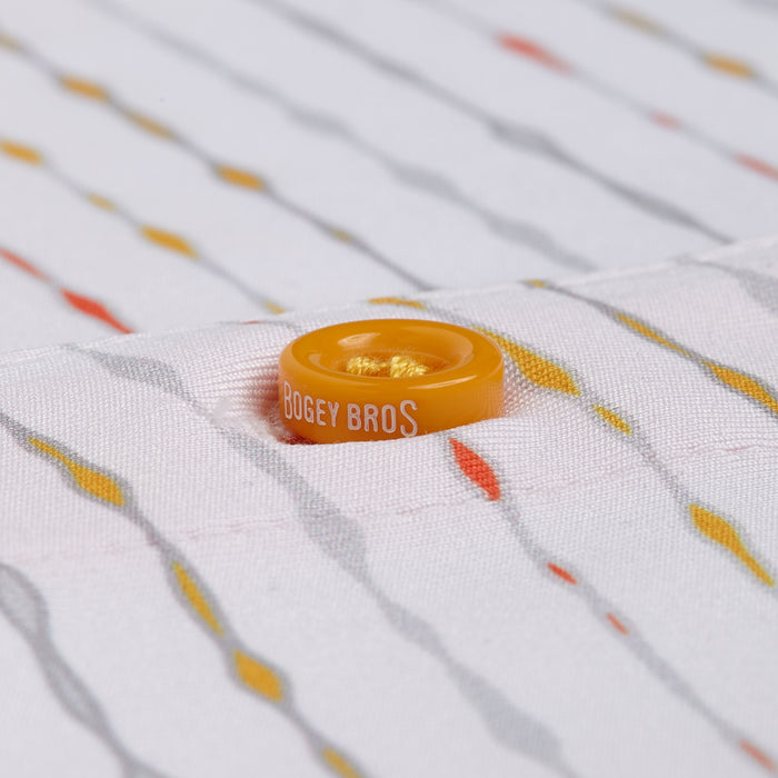 Close-up of a yellow-orange BOGEY BROS button on the Heat Index - Polo’s white, moisture-wicking fabric featuring diagonal grey, orange, and yellow lines. The sharp image highlights the fabric’s texture and thread details.
