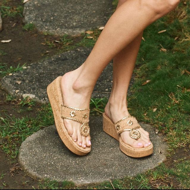 Tan cork sandals with gold embellishments worn outdoors on a concrete surface.