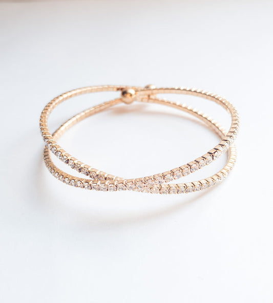 A sparkly gold cuff bracelet with a crossover design, displayed on a white background.