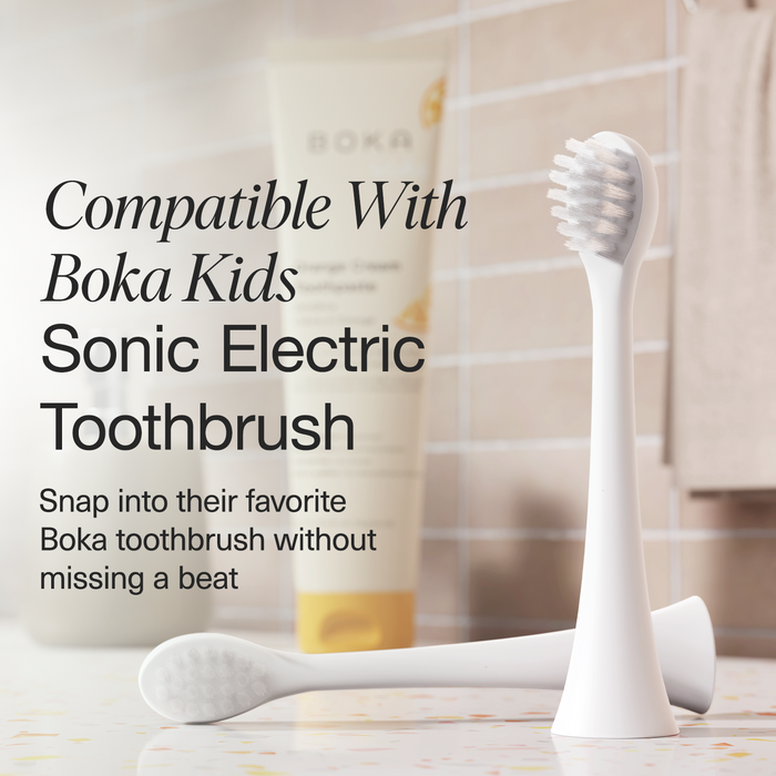 Two white Replacement Heads for Kids Sonic Toothbrush stand upright on a bathroom counter.