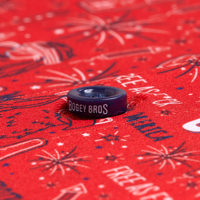 Close-up of a purple BOGEY BROS button on the 'Merica - Red - Polo, featuring bright red, moisture-wicking fabric with blue and white fireworks, popsicles, and festive summer patterns—perfect for active summer days.