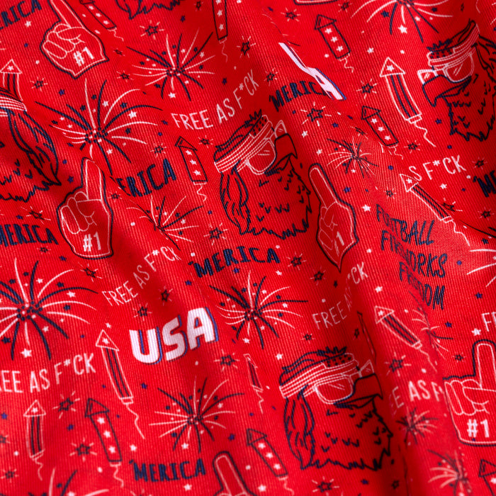 A close-up of 'Merica - Red - Polo: red fabric with white and blue patriotic designs—fireworks, rockets, #1 foam fingers, sunglasses, bold phrases—and UPF 50 protection for sun safety.