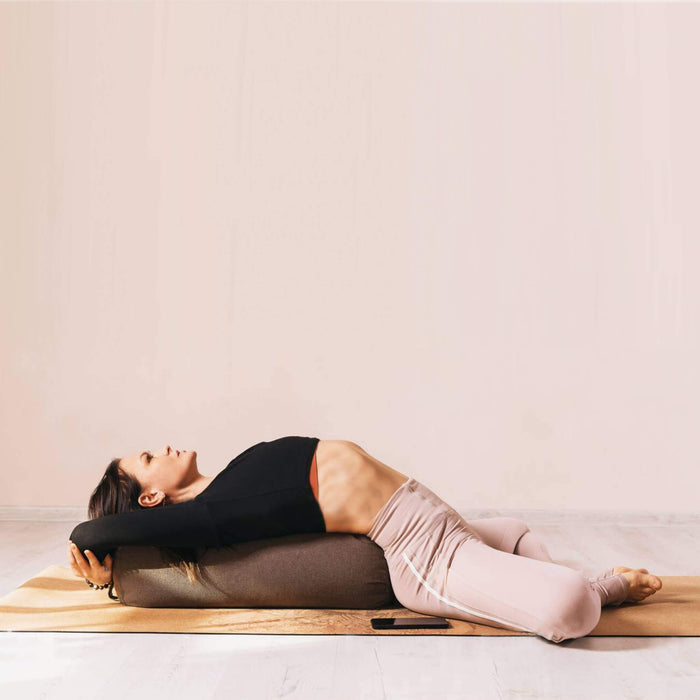 A woman laying down on yoga bolster and a cork yoga mat