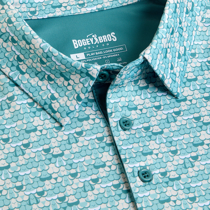 Close-up of the T&A - Luscious - Polo, a teal collared shirt with a scale pattern in blue and white. Features a “BOGEY BROS GOLF” tag (size L), moisture-wicking fabric, and a button-down front with three teal buttons.