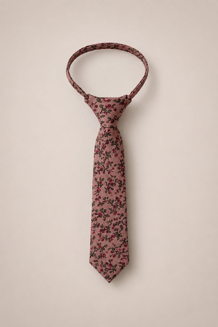 The Ivy City Co Ties in Mauve Woodland Floral features a pink cotton necktie adorned with a dark red and green woodland floral pattern, shown on a plain light beige background—an elegant accessory ideal for weddings.