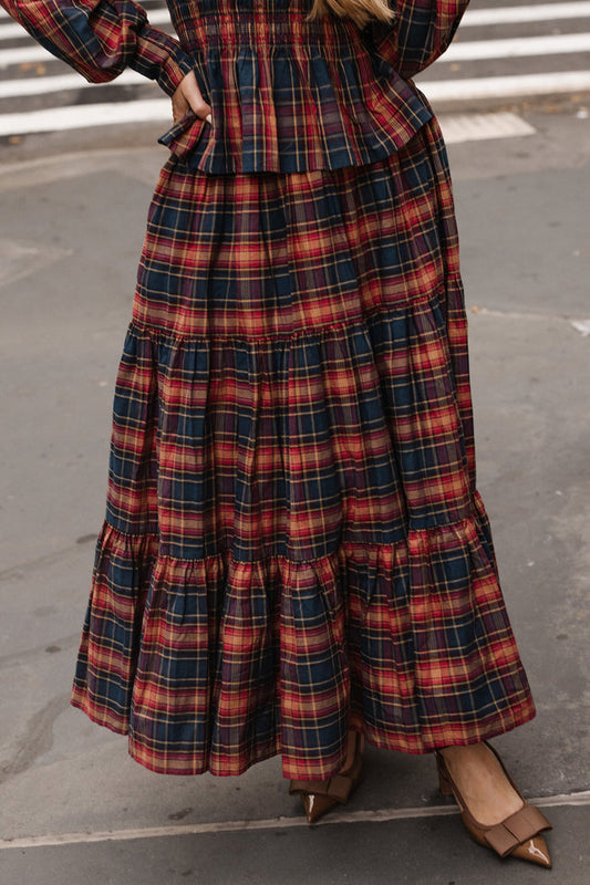 A person stands on a city sidewalk, their lower half visible in the Zoey Skirt in Twilight Plaid by Ivy City Co—a striking mix of red, navy, and yellow plaid styled with brown pointed-toe shoes for effortlessly chic fall fashion.