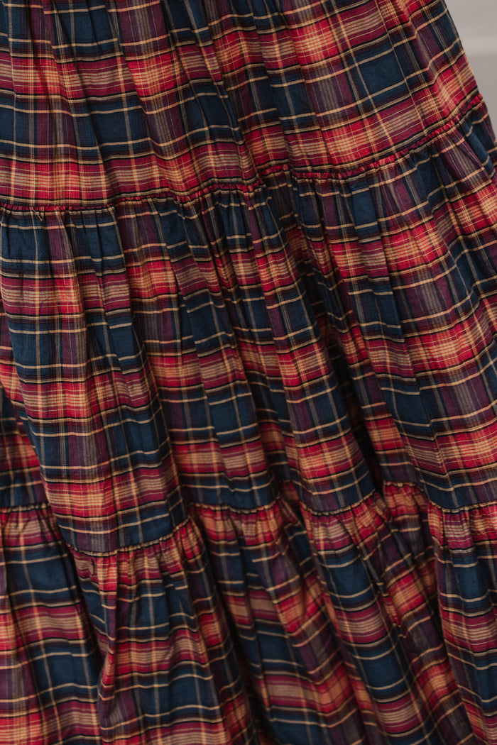 Close-up of the Zoey Skirt in Twilight Plaid by Ivy City Co—a tiered cotton A-line skirt featuring a dark blue, red, and yellow plaid pattern. The fabric is gently gathered at the seams for added texture, making it a perfect choice to bring timeless charm to your fall fashion collection.